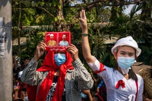 Pengunjuk rasa memberi hormat dengan tiga jari saat yang lain memegang poster yang menampilkan gambar pemimpin de-facto Aung San Suu Kyi selama pawai anti-kudeta pada 6 Februari 2021 di Yangon, Myanmar. (getty images)