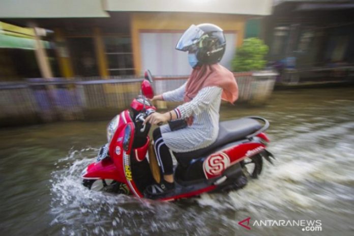 Pengedara menerobos genangan akibat air sungai pasang tinggi meluber hingga ke jalan. (antara)