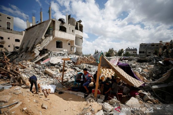 Warga Palestina duduk di tenda darurat di tengah puing-puing rumah mereka yang dihancurkan oleh serangan udara Israel selama pertempuran Israel-Hamas di Gaza, Minggu (23/5/2021). REUTERS/Mohammed Salem/RWA/sa.